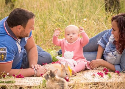 A family enjoying a picnic outdoors with their baby and rabbits.