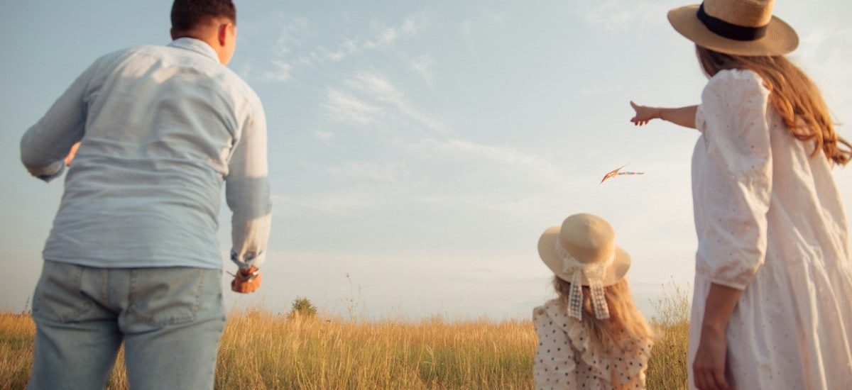 A family in a field flying a kite under a clear blue sky